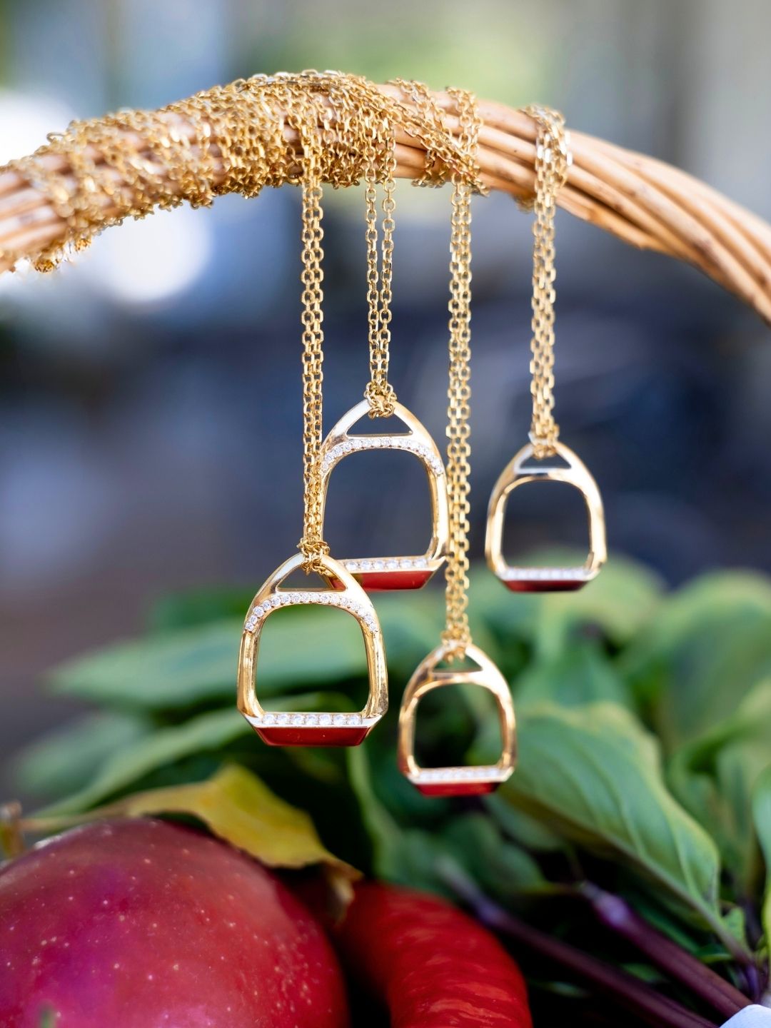 Grouped stirrup necklaces above apples and foliage in a wicker basket