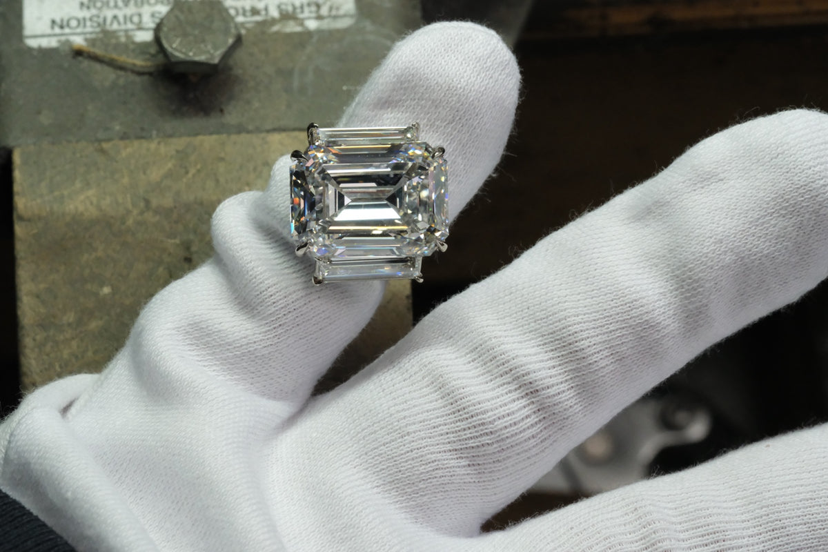 Platinum emerald-cut diamond ring with tapered baguette side stones, shown on a gloved hand